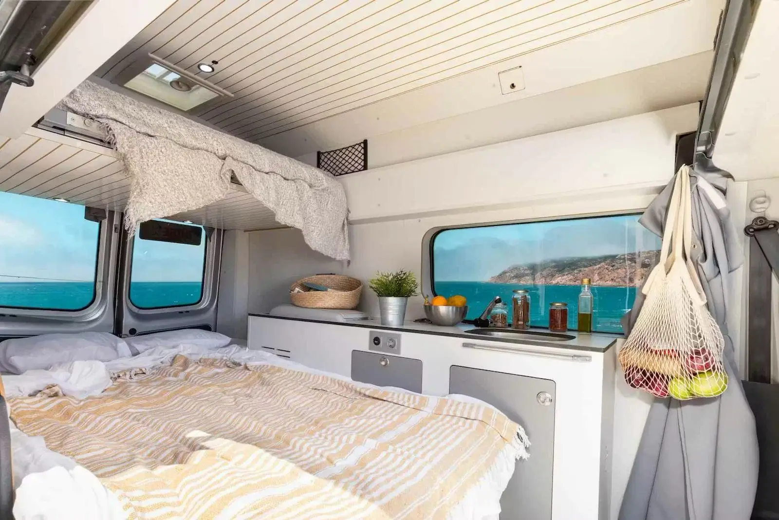 Bed made up in the Fiat Talento campervan with the kitchen alongside and the sea outside