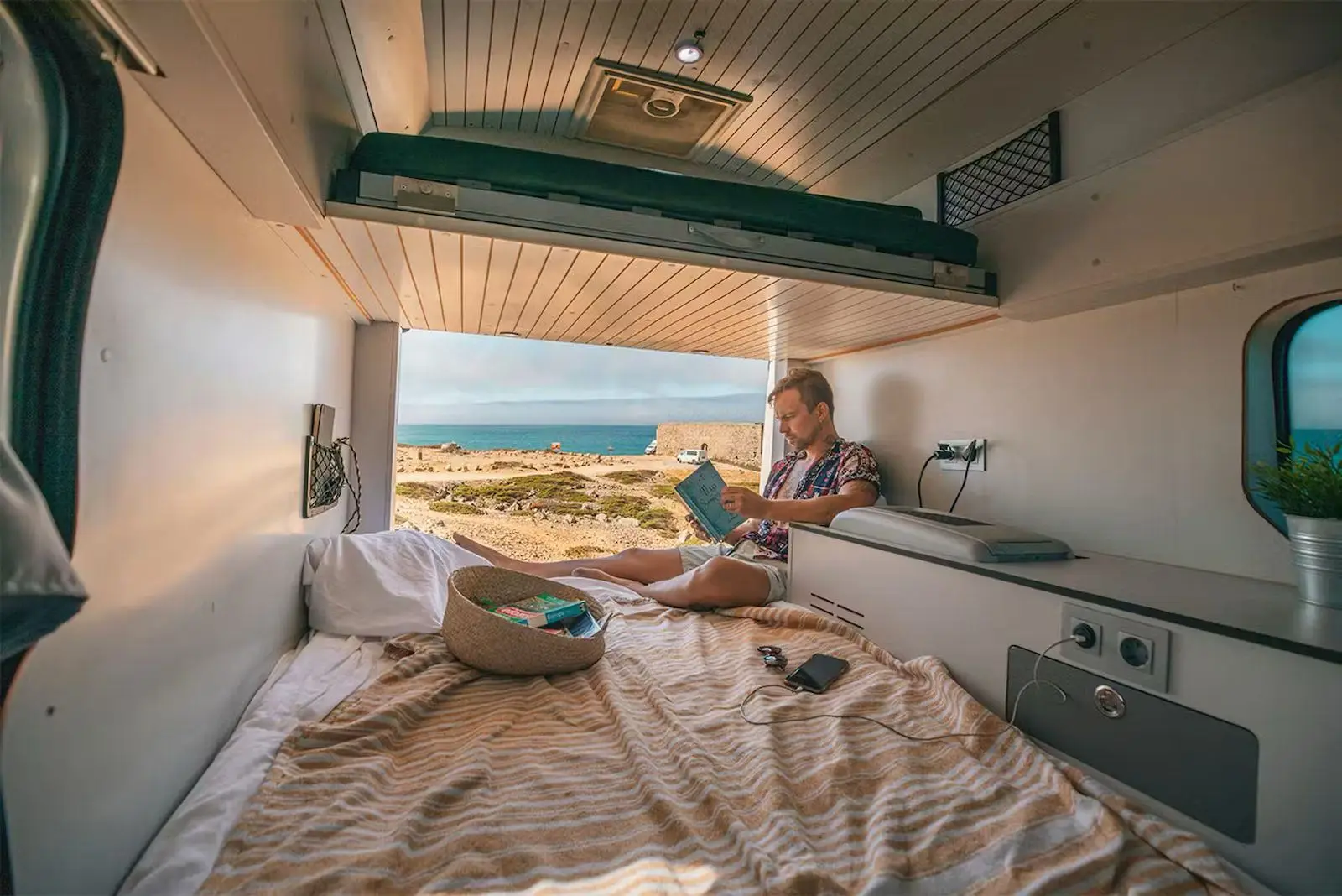 Someone lying on the bed of the Fiat Talento campervan, rear doors open to the coast