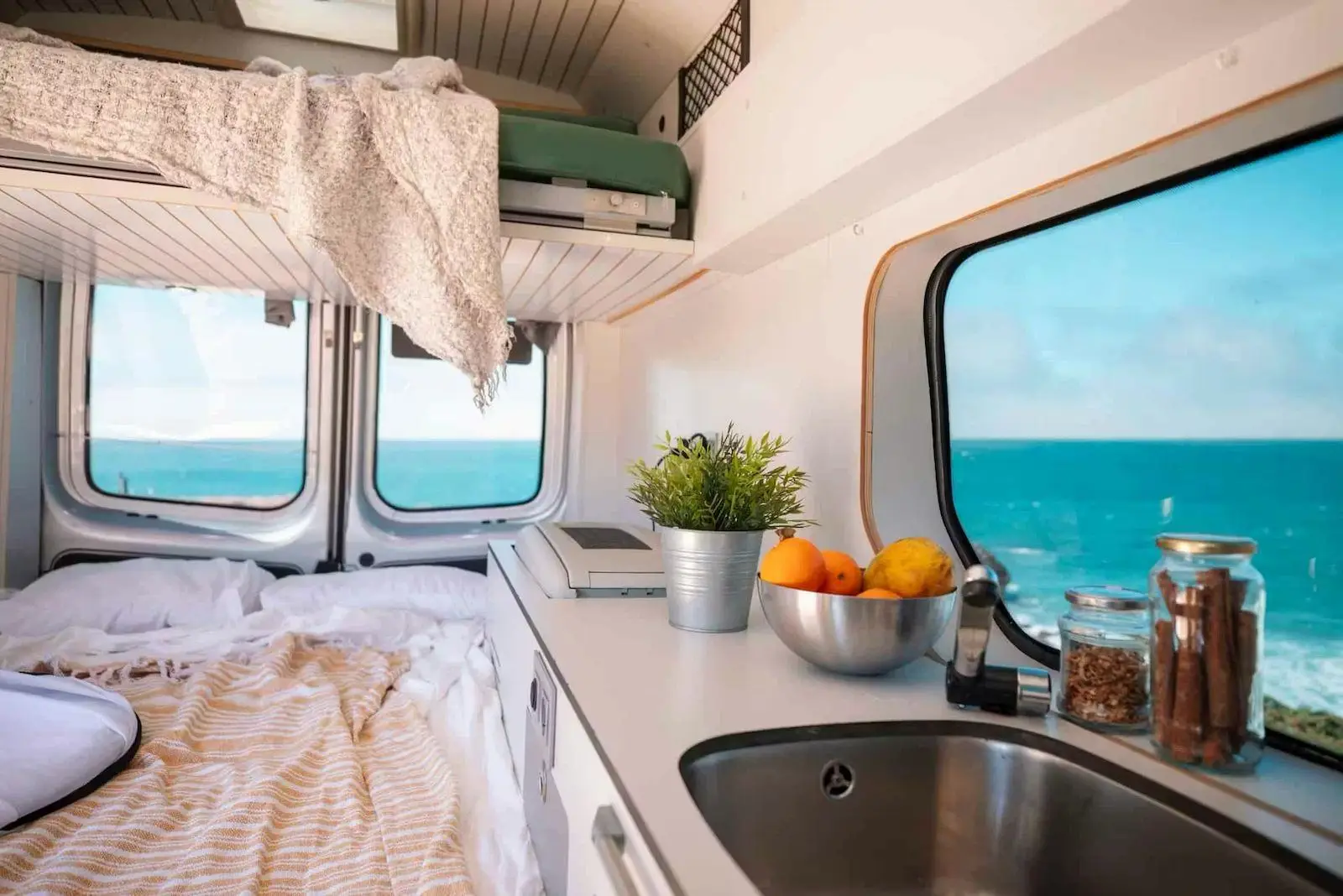 Bed and kitchen sink in the Fiat Talento campervan, the sea beyond the window