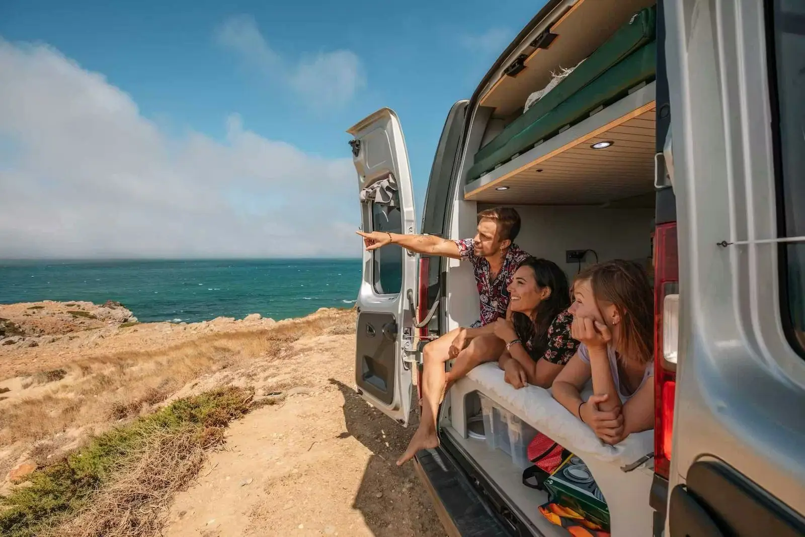 Four people sitting in the open rear doors of the Fiat Talento campervan on a clifftop